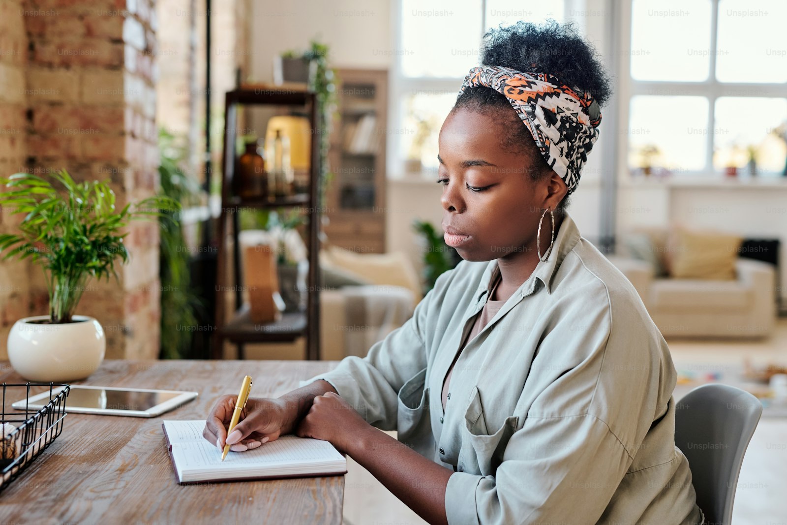 African American woman writing notes with a pen in her planner at a wooden desk